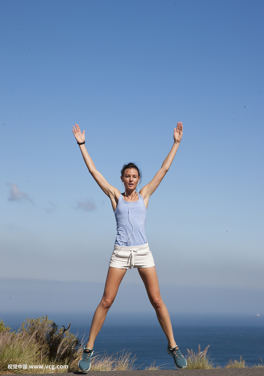 Sport Woman Jumping Mid-air against Ocean and Blue Sky